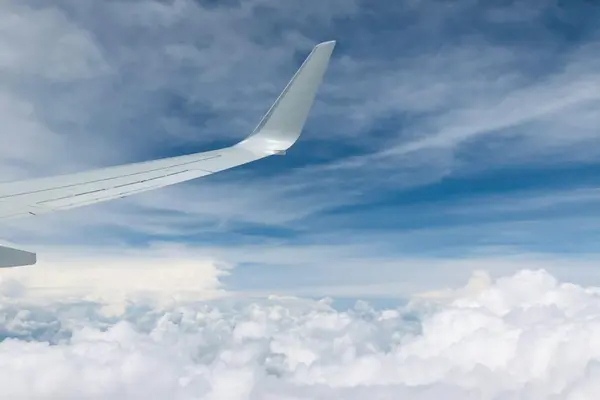 An airplane wing above the clouds in a blue sky