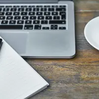 A laptop, an open notebook with a pen, and a coffee on a desk